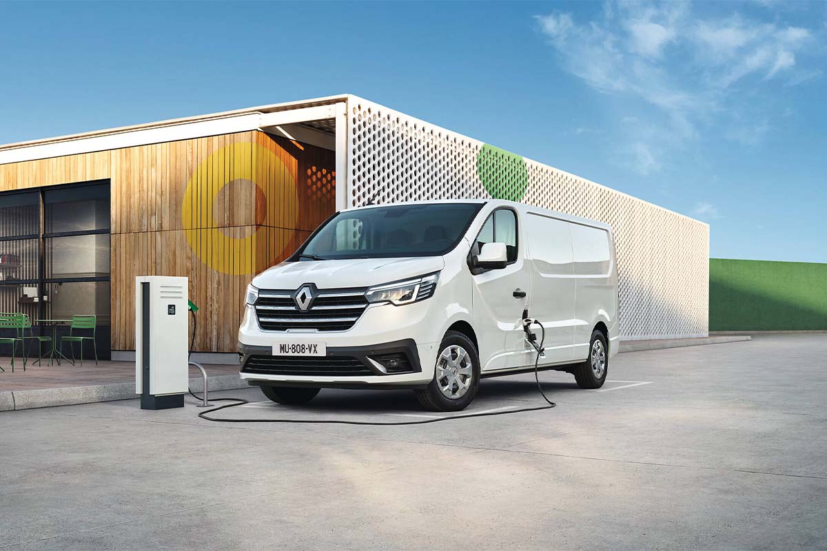 Grafik: Renault Trafic E-Tech Electric vor einer Lagerhalle, ist an einem Ladekabel angeschlossen