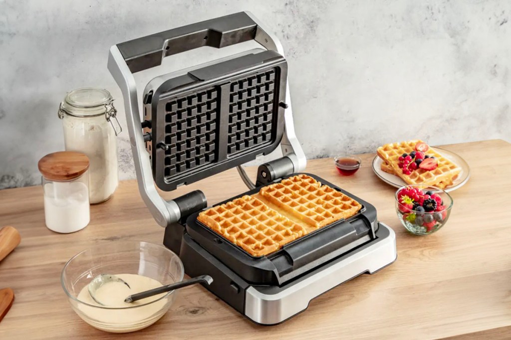 Der Tefal-Kontaktgrill "OptiGrill 4in1" mit Waffelplatten und Backzubehör auf einem Tisch.