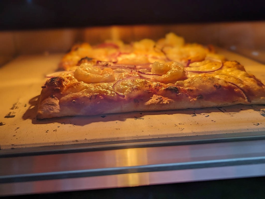 Ein Blick durch die Scheibe des Ooni. Dahinter liegt eine Pizza.