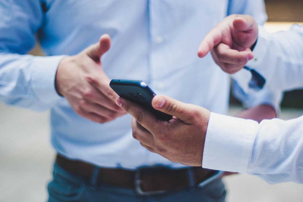 Zwei Männer in blauen Hemden zeigen auf ein Smartphone.