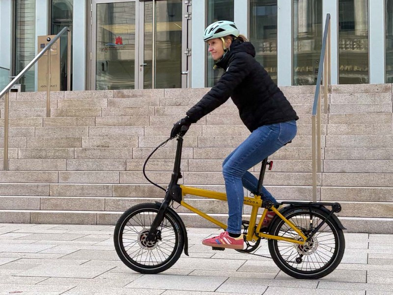 Frau fährt auf einem gelben Falt-E-bike über einen Platz