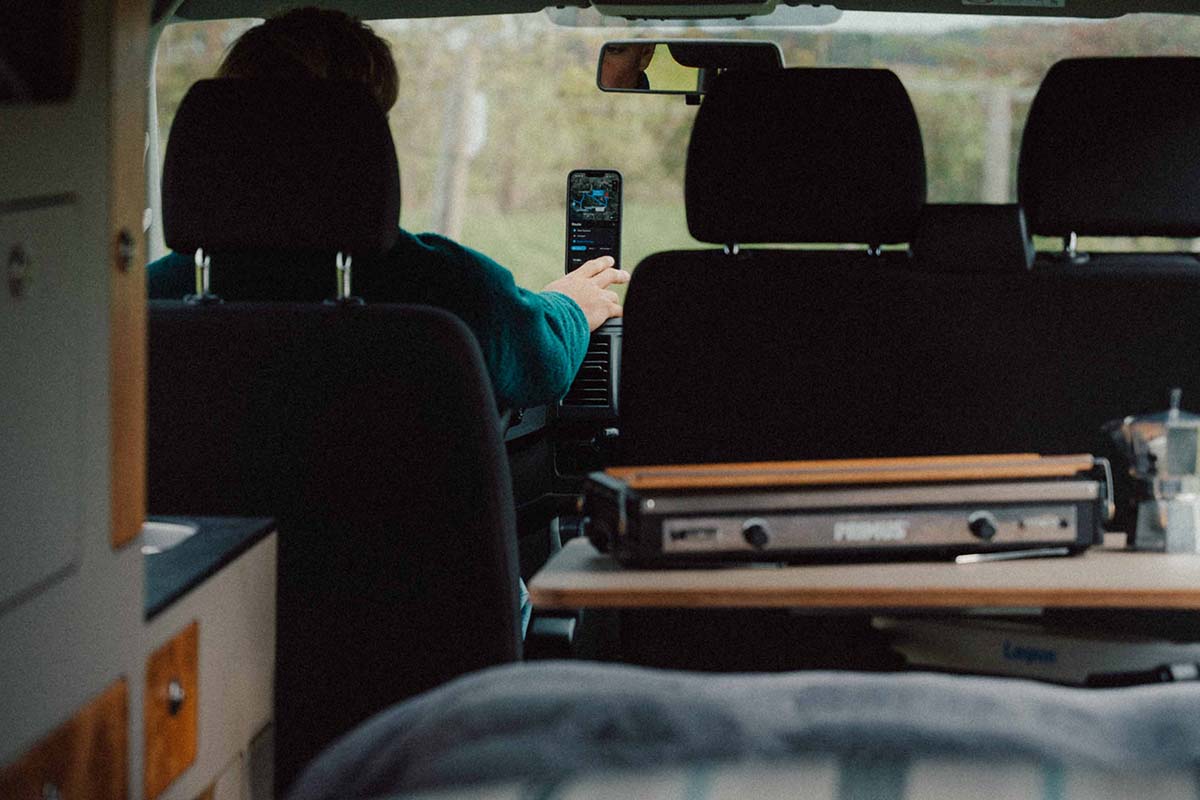 Blick von Heck eines Wohnmobils nach vorne raus, man sieht, dass eine Person mit dem Finger auf ein Smartphone tippt, welches an der Windschutzscheibe befestigt ist