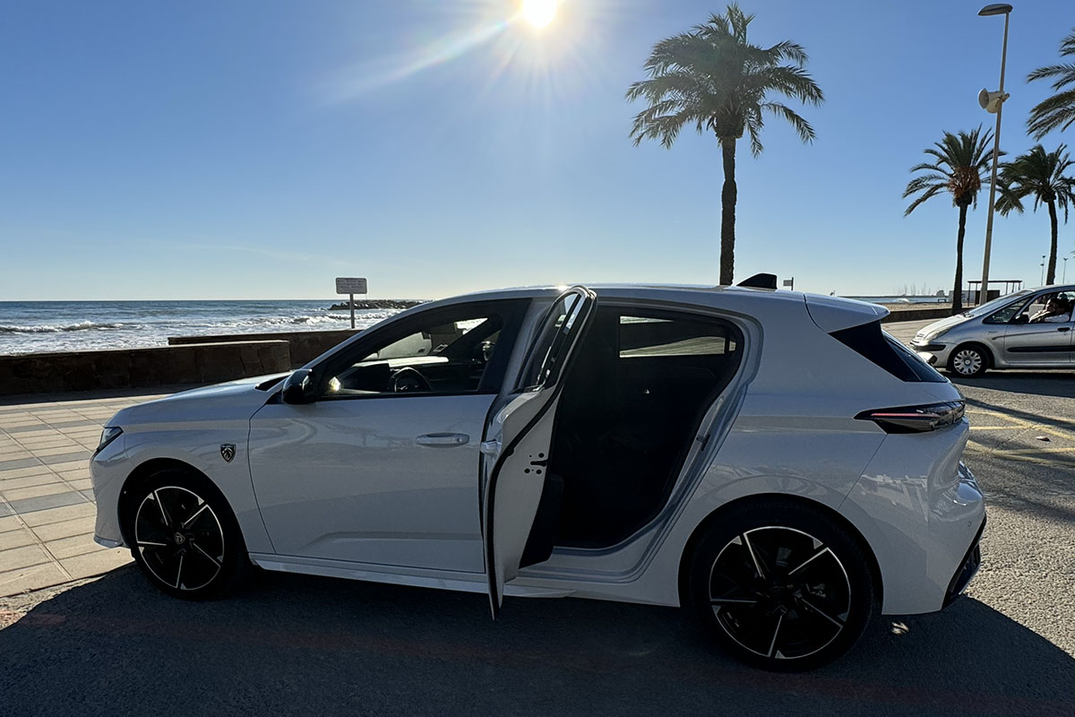 E-Auto Peugeot E-308 von außen vor Meeresprommenade fotografiert – Seitenansicht mot geöffneter Hintertür.