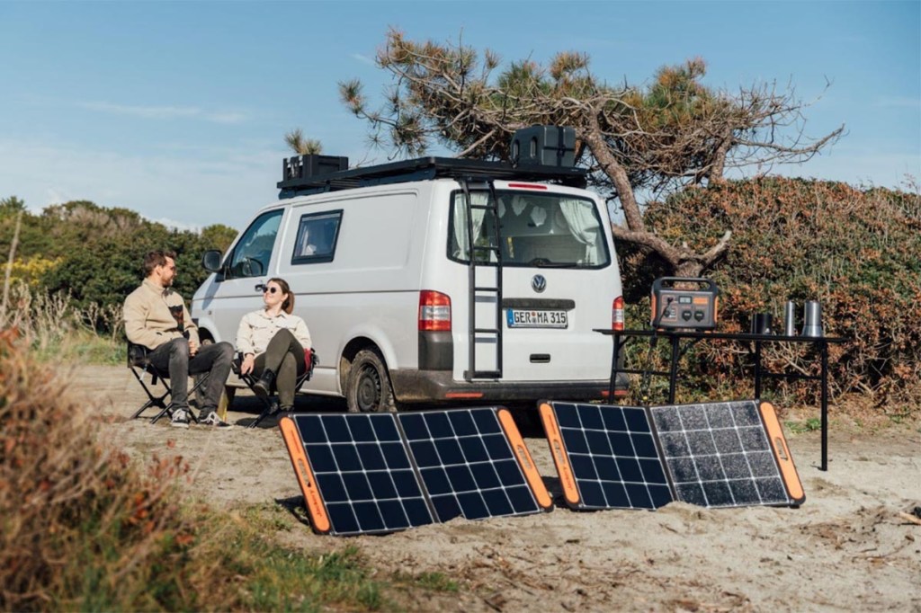 Ein Paar sitzt in der Natur vor einem Camper, vor dem Solarpanel stehen