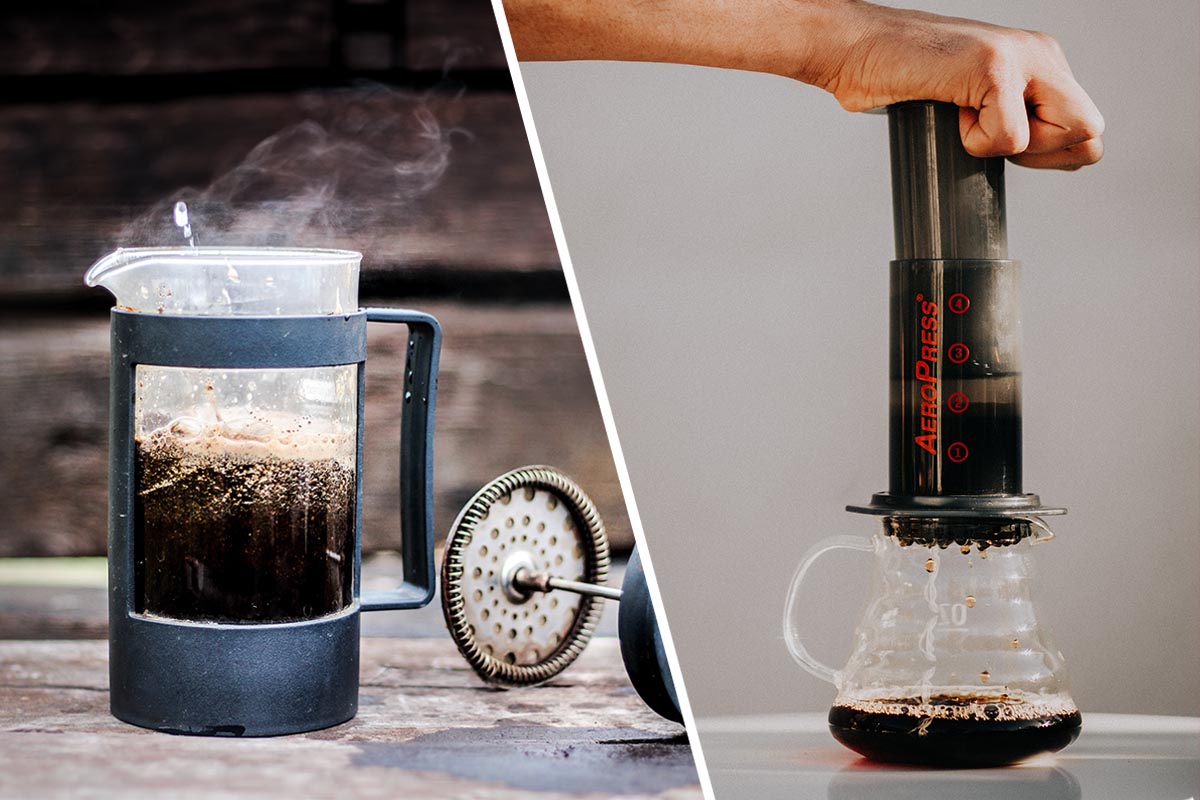 Links offene French Press Kanne aus Glas mit dampfend heißem Kaffee in schwarzem Kunststoffrahmen auf heller Fläche vor dunkler Wand, rechts Hand die dunkle Aeropress über Glasbecher hält in dem Kaffee tropft