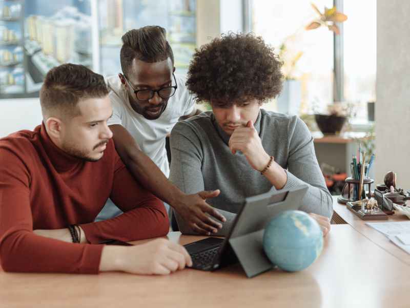 Drei junge Männer in einem Büro auf ein Tablet schauend