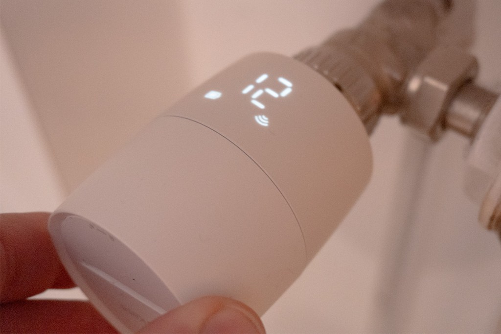 Eine Hand dreht am TP-Link-Thermostat; die Temperaturanzeige leuchtet.