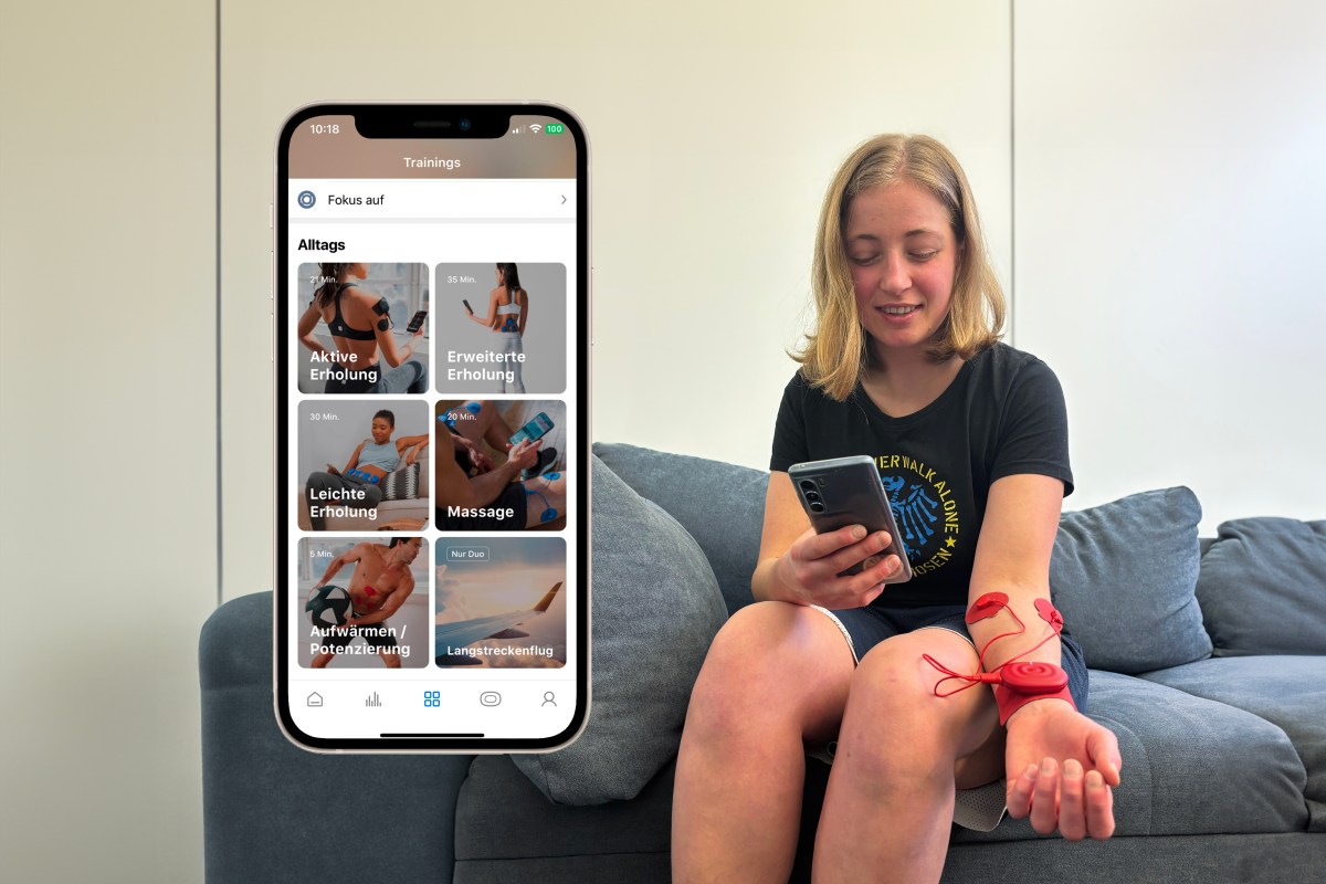 Eine blonde Frau sitzt. mit dem roten Powerdot am Arm auf einem grauen Sofa. Davor ist ein Screenshot der passenden App zu sehen.