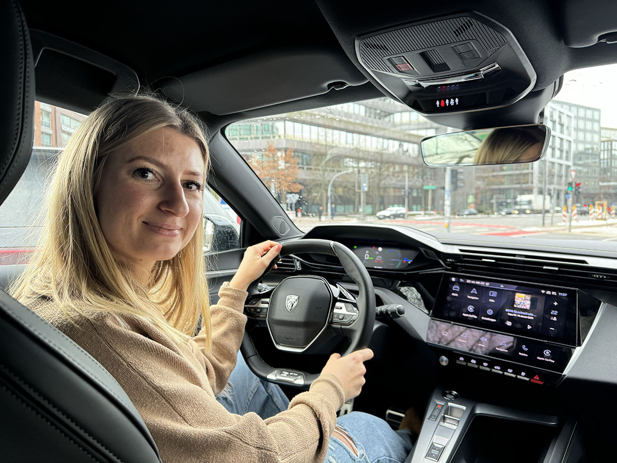 Lächelnde Frau in E-Auto mit Schulterblick auf die Rückbank.