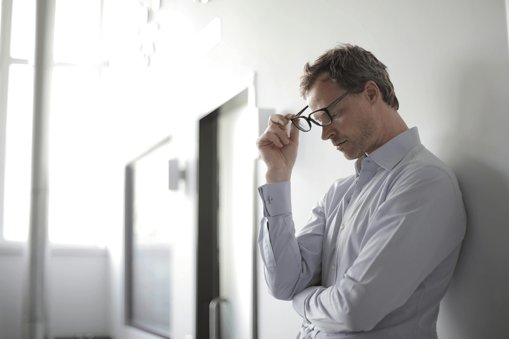 Ein gestresster Mann fasst sich an die Brille.