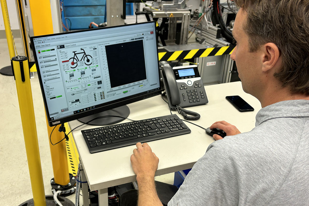 Mann sitzt an einem Schreibtisch vor einem PC und trägt Messdaten für eine Labor-Prüfung eines E-Bikes in ein Datenblatt ein.