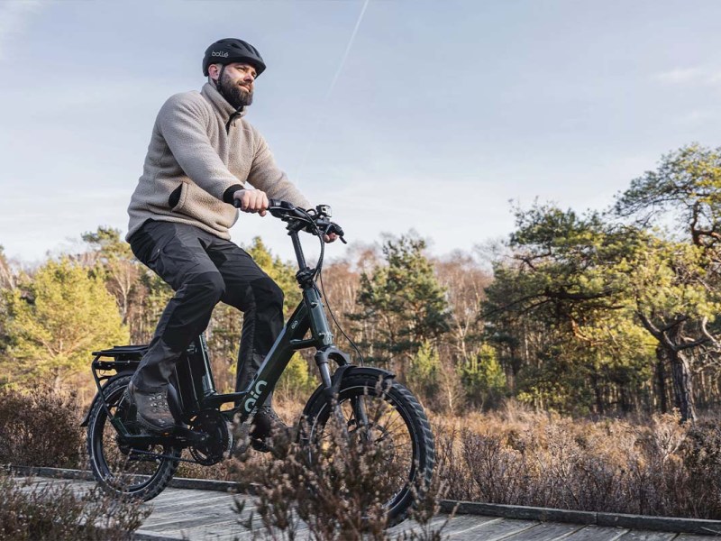 Mann fährt mit einem Kompakt-E-Bike über einen Holzsteg, der durch eine Waldlandschaft führt