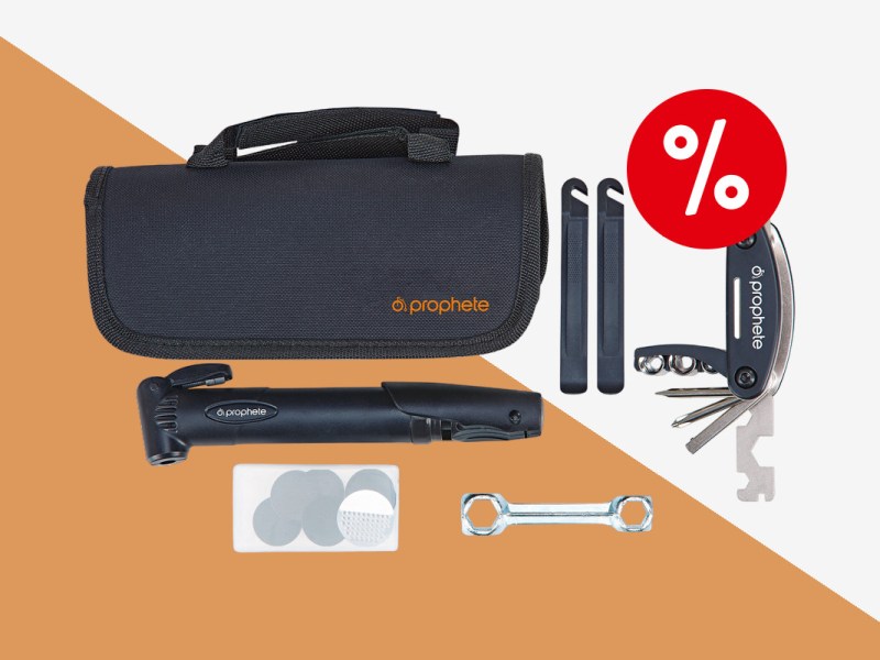 Fahrradwerkzeug Set bestehend aus schwarzer länglicher Tasche oben links, dadrunter einer schwarzen Miniluftpumpe, daneben zwei schwarze längliche Werkzeuge und ein aufgefächertes Multitool mit rotem Prozentbutton oben rechts auf orange weißem Hintergrund