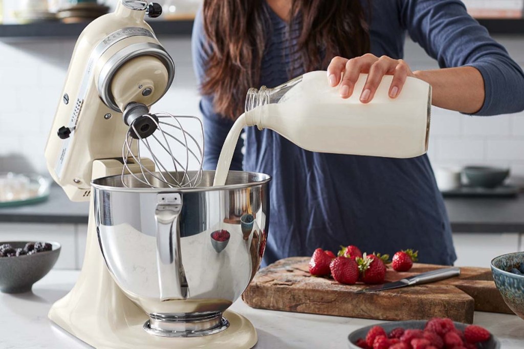 Person im Anschnitt, sie schüttet Milch in eine Rührschüssel einer Küchenmaschine