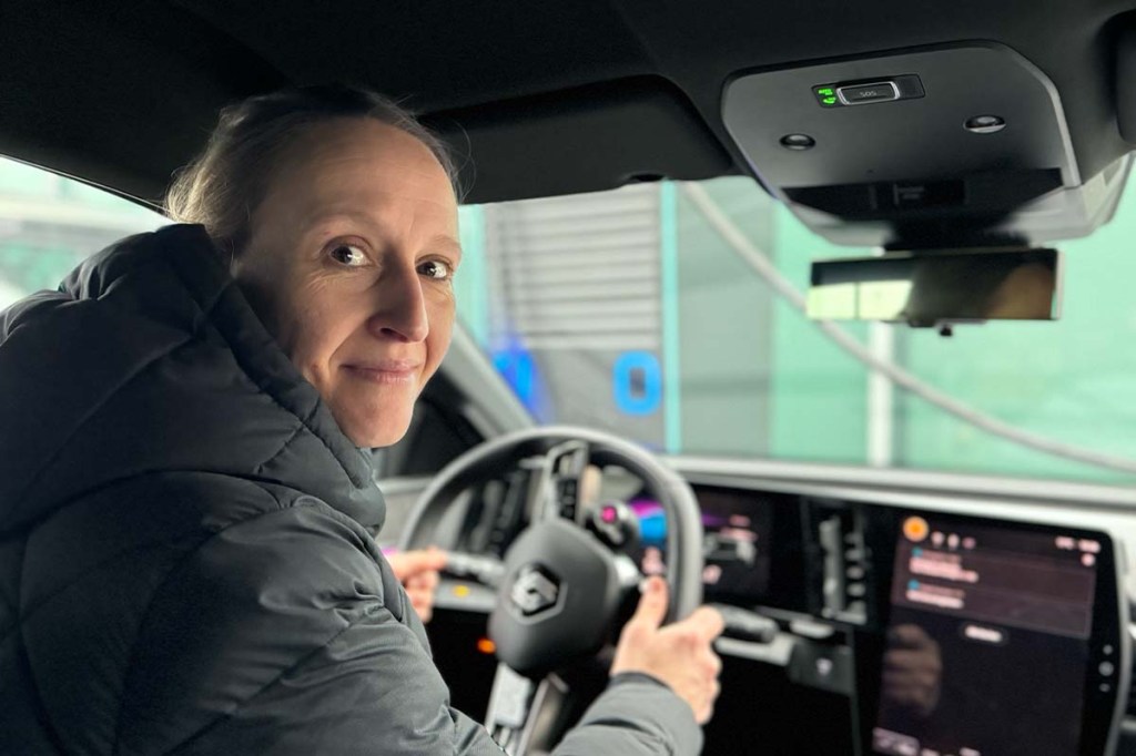 Frau schaut, auf dem Fahrersitz eines Auto sitzend, nach hinten zur Rückbank, Blick aus Sicht des auf der Rückbank sitzenden