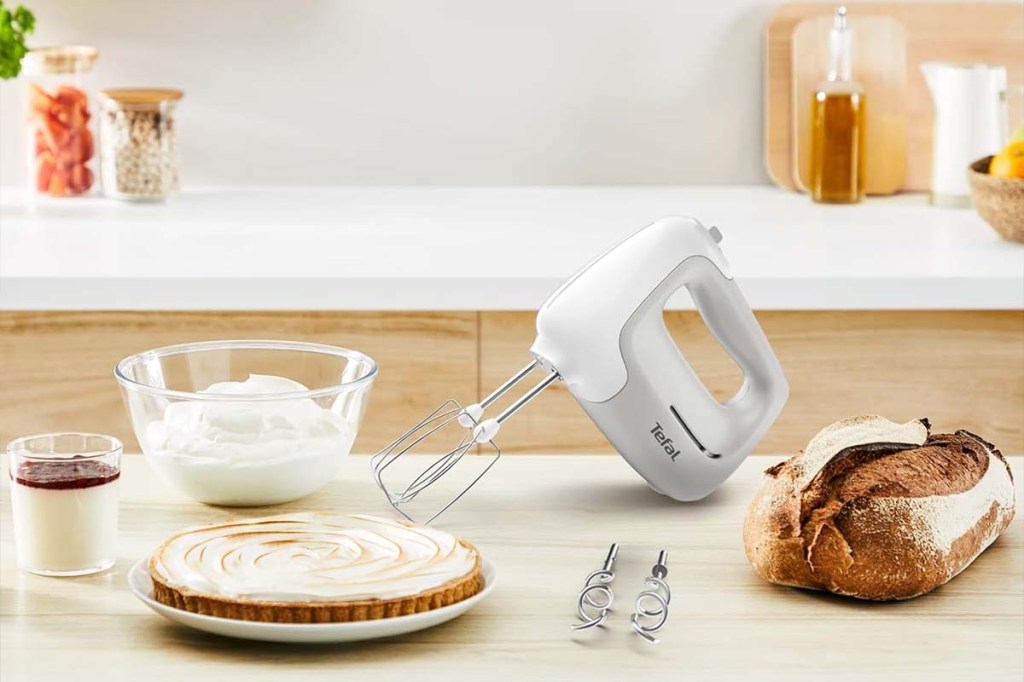 Handmixer auf einer Arbeitsplatte stehend, daneben ein Brot, ein Kuchen und eine Creme