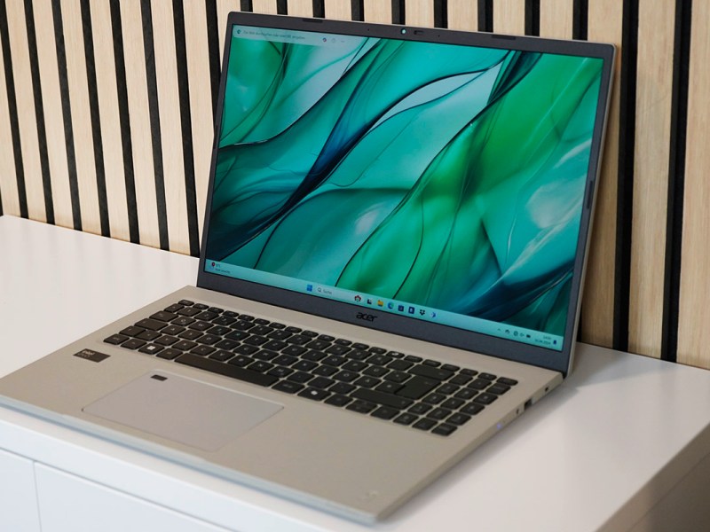 Das Notebook Acer Aspire Vero 16 steht auf einem weißen Sideboard vor einer hellen Holzwand.