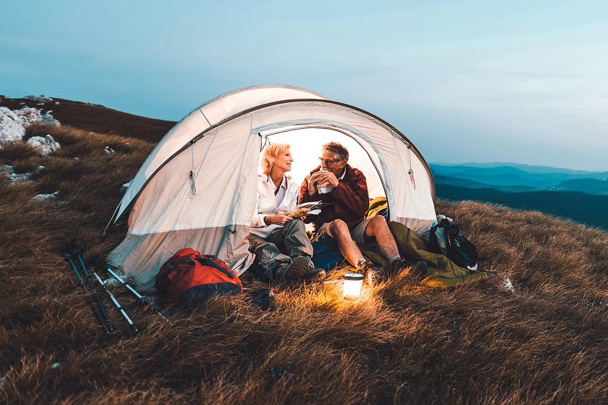 Ein älteres Pärchen sitzt in der Natur im Zelt während es dämmert.