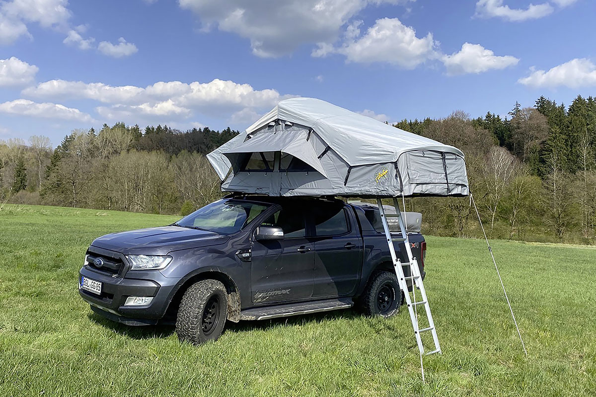 Dachzelt von Gordigear auf einem SUV montiert, der auf einer Wise vor einem Waldstück steht.