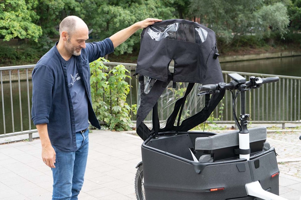 Mann hält Regenverdeck von Cargo-E-Bike hoch, um in die Transportwanne zu schauen