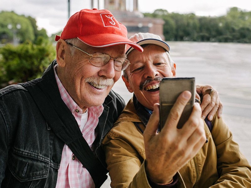 Zwei ältere Männer mit einem Smartphone in der Hand unter freiem Himmel.