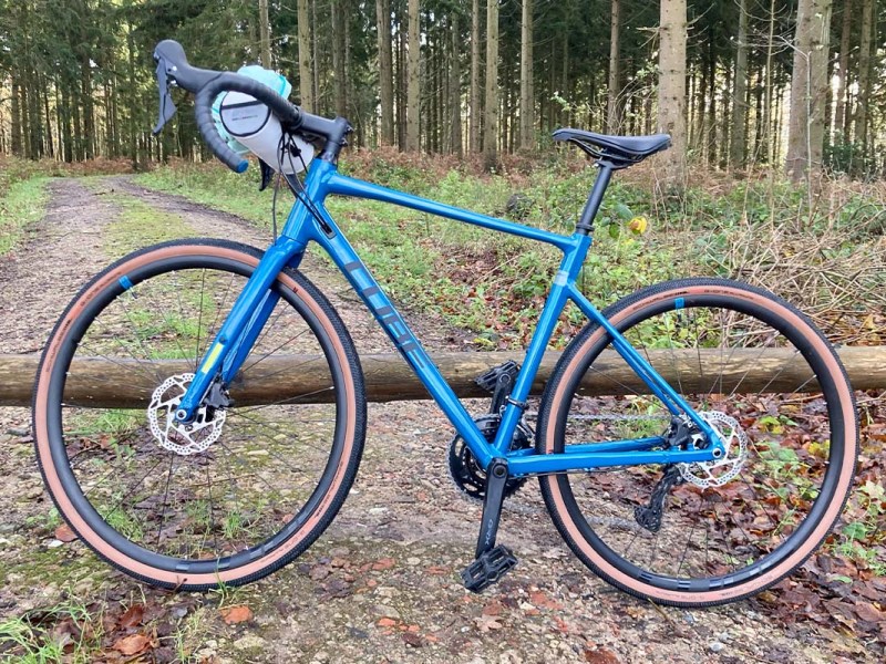 blaues E-Bike lehnt vor einer Baumschranke, Wald im Hintergrund