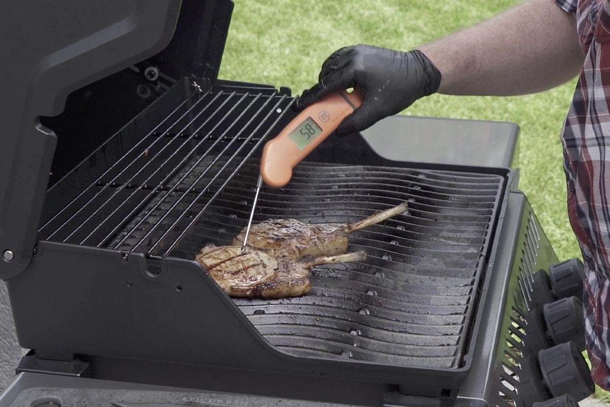 Zwei Stück Fleisch deren Temperatur gemessen wird auf einem Gasgrill.