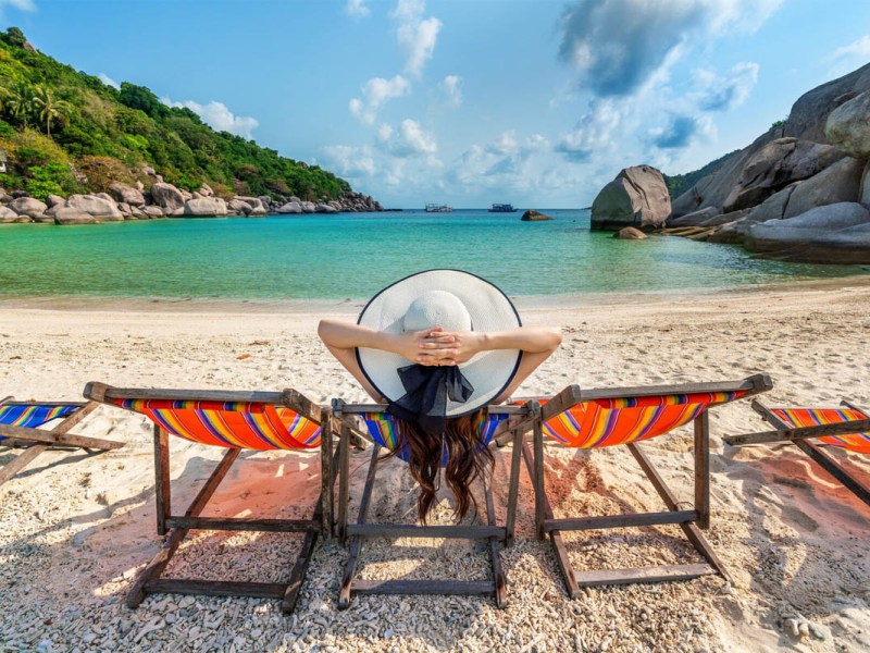Eine Frau liegt mit Sonnenhut in einem Liegestuhl am Strand.