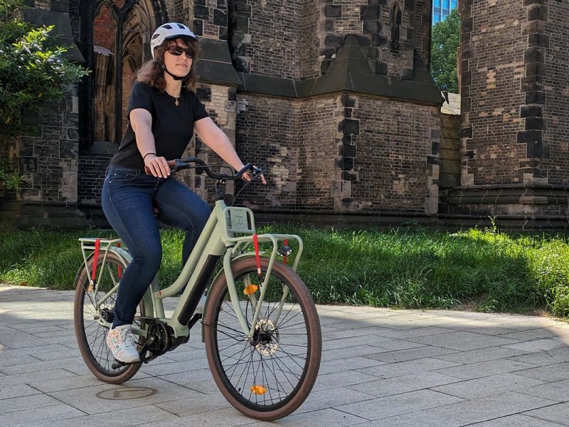 Frau fährt mit einem Fahrrad über einen Platz, Kirche im Hintergrund