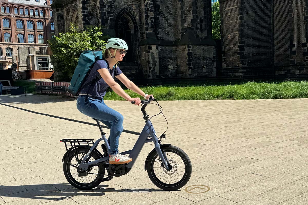 Frau fährt mit einem E-Bike über einen Platz, Kirche im Hintergrund