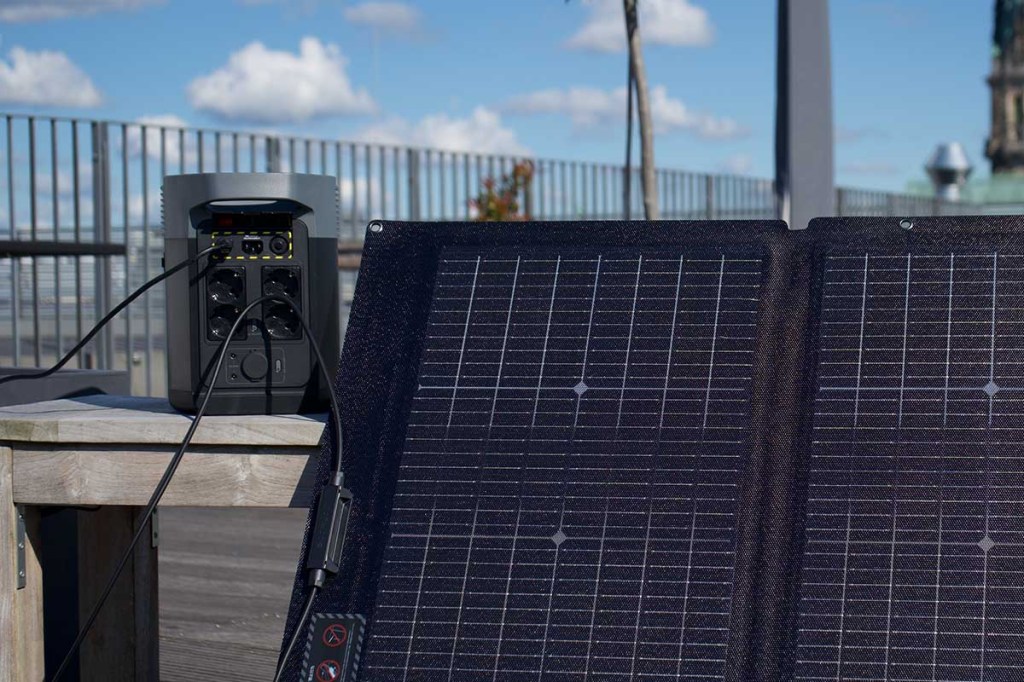 Die Delta 2 auf einem Holztisch auf einer Dachterrasse. Davor ein Solarpanel.