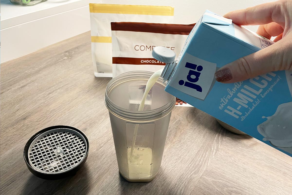 Eine Hand füllt Milch in den geöffneten Juice Plus+ Shaker.
