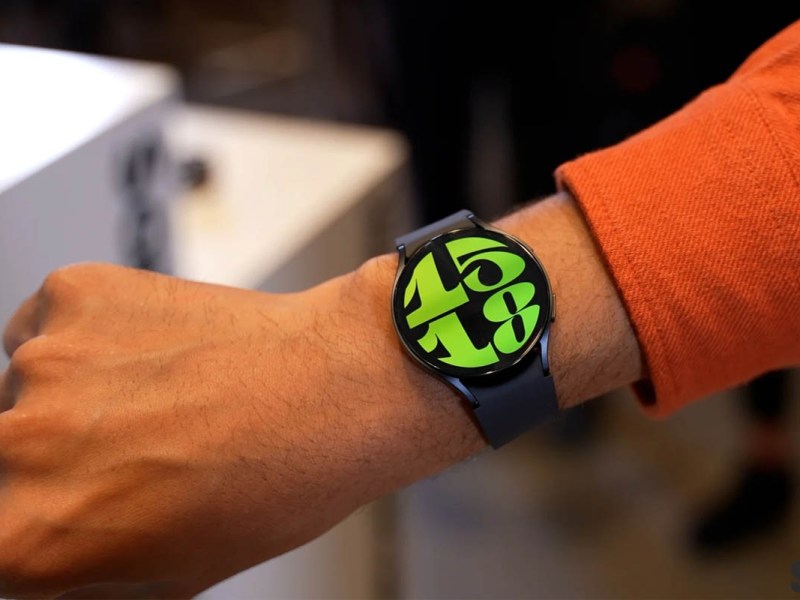Eine Galaxy Watch 7 mit grünen Zahlen an einem Arm mit orangem Ärmel.