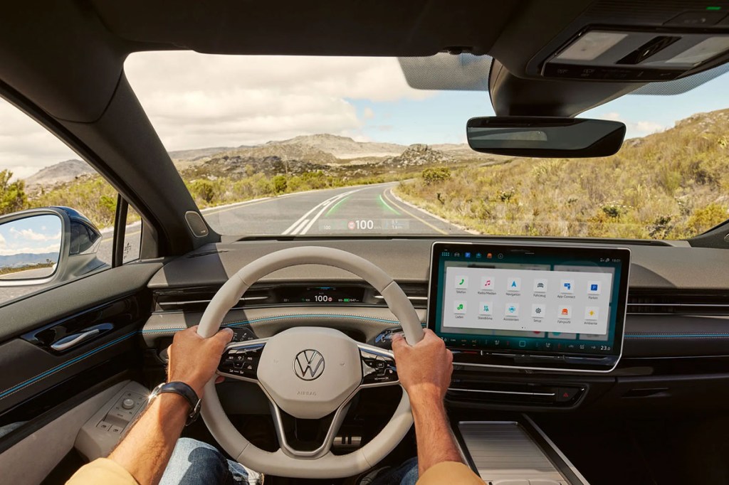 Blick durch die Windschutzscheibe des VW ID.7 auf eine hügellige Straße. Eingeblendet sind Abbiegehinweise und Tempoanzeige über ein Head-up-Display.