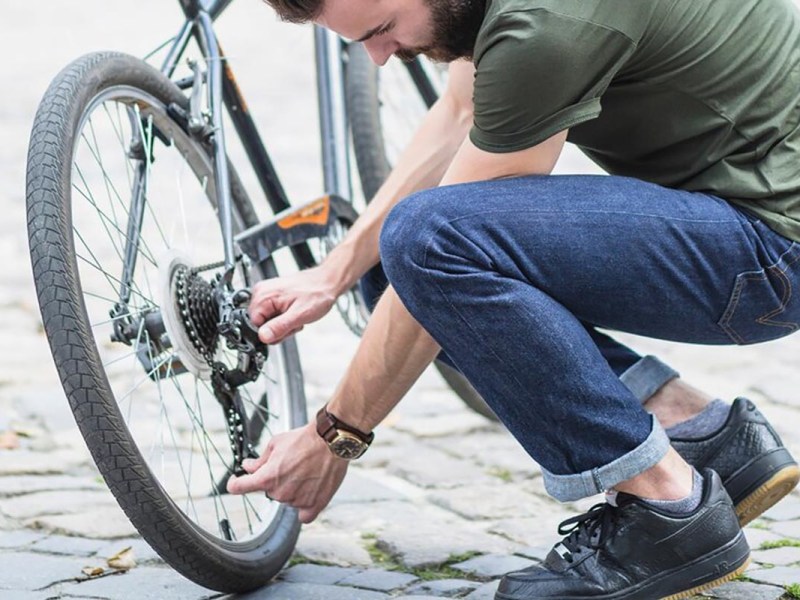 Person hockt neben einem Fahrrad mit den Händen an der Kette.