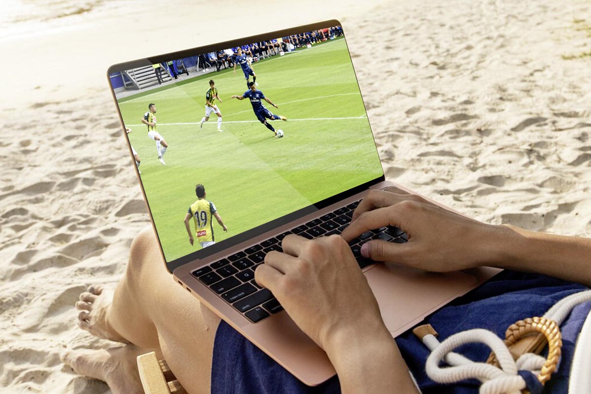 Person guckt am Strand auf einem Laptop Fußball.