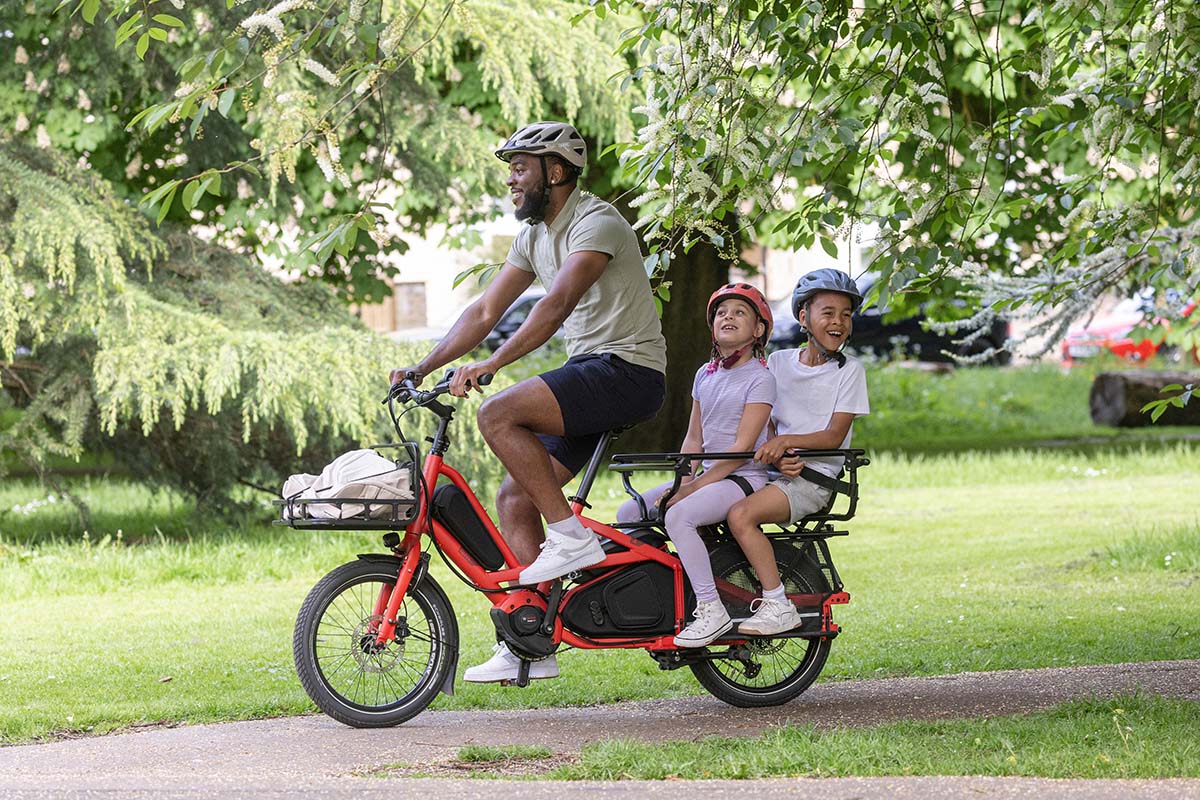 Mann auf einem kompakten E-Lastenrad, zwei Kinder auf dem Rücksitz