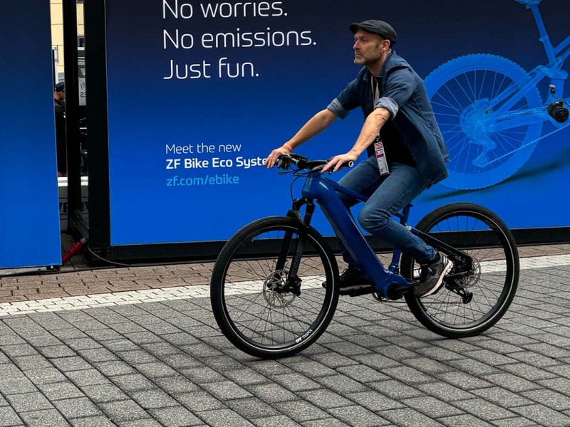 Mann fährt mit einem E-Bike, hinter ihm ein blaues Werbeplakat