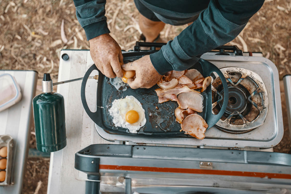 Ein Mann macht rustikale Spiegeleier auf einem Campingkocher.