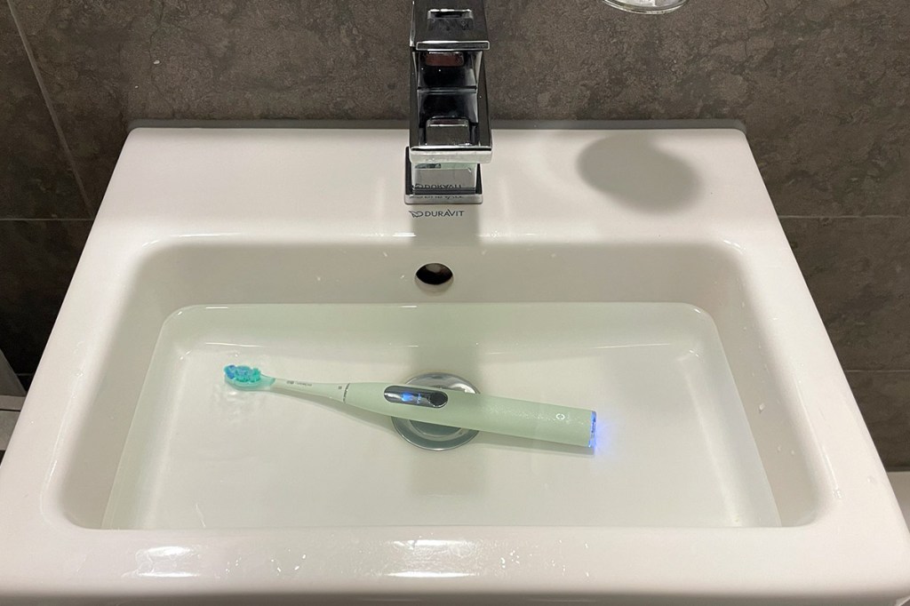 Eine grüne, elektrische Zahnbürste in einem Waschbecken mit Wasser.