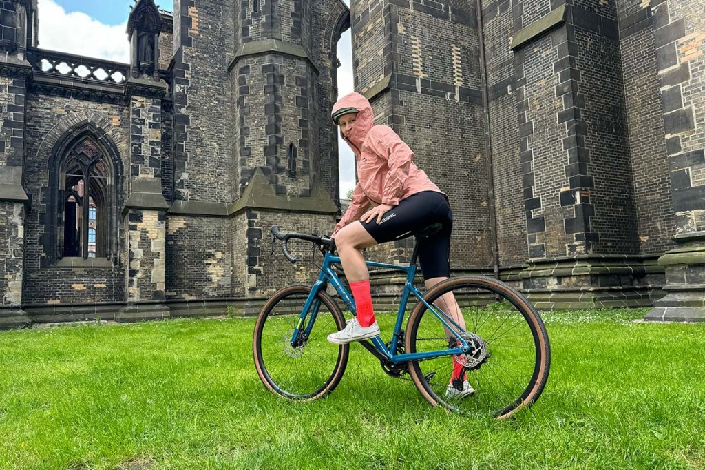 Totale, Frau von hinten, sitzt auf einem Fahrrad und hat eine REgenjacke an