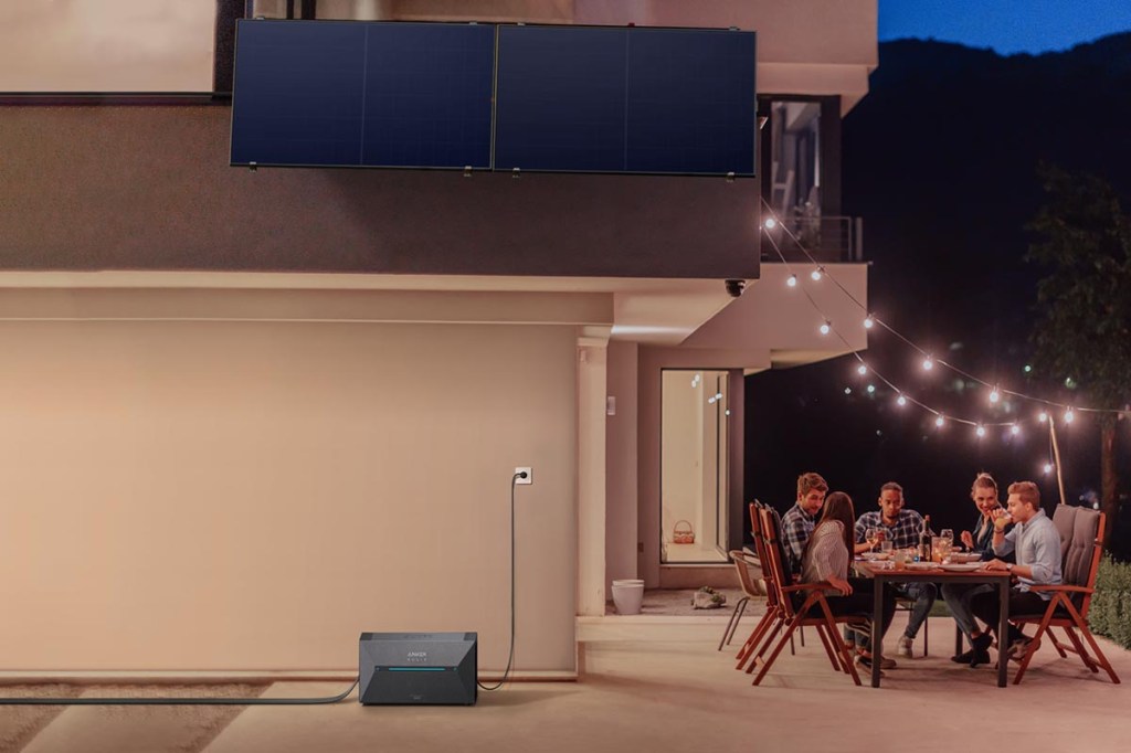Die Anker Solix Solarbank 2 Pro auf der Terrasse, während ein paar Freunde am Abend auf der Terrasse am Tisch zusammensitzen.
