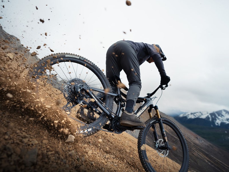 Mann fährt rasant bergab mit einem E-Mountainbike, so dass Sand und Steine herumwirbeln.