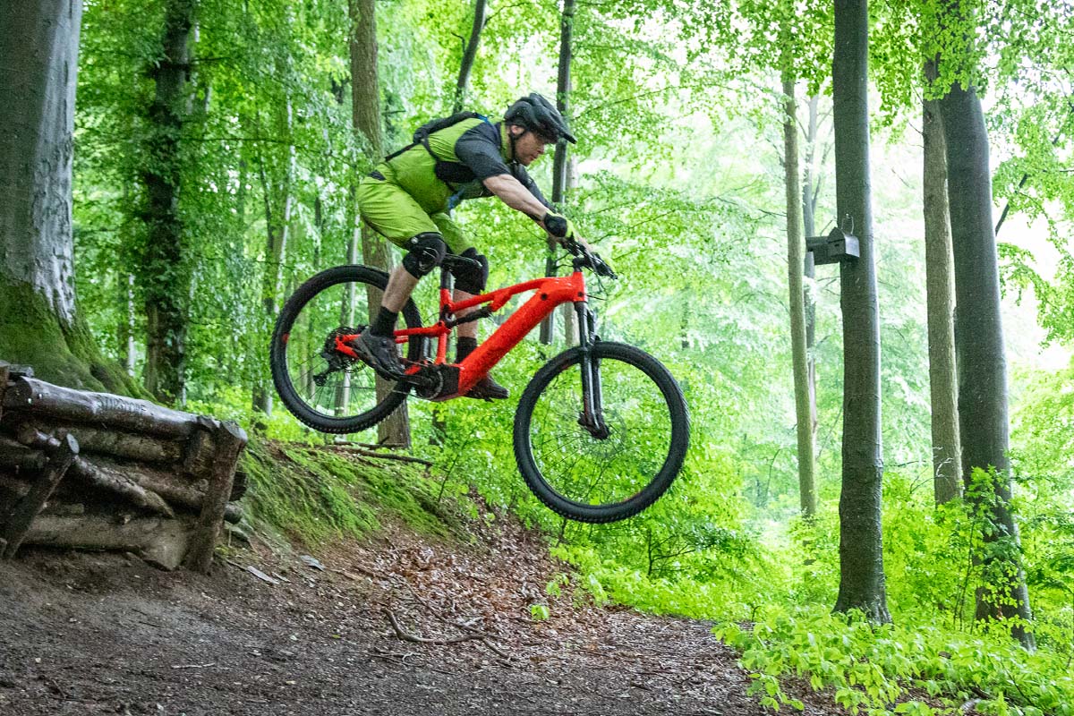 Mann springt mit seinem E-Mountainbike über eine SChanze im Wald