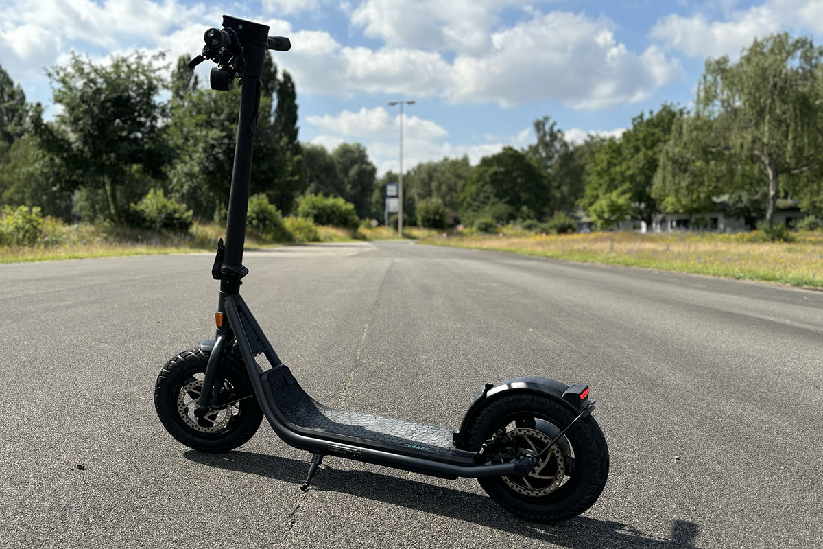 E-Scooter in Profilansicht auf Straße vor Wald-Landschaft.