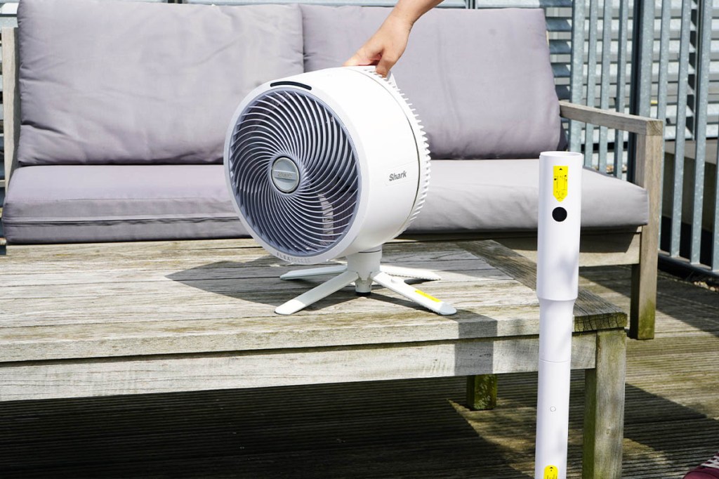 Eine Person stellt den Shark FlexBreeze als Tischventilator auf einen Gartentisch. Der Standfuß steht daneben.