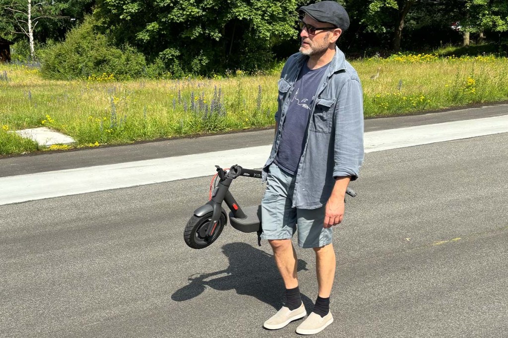 Mann trägt zusammengeklappten E-Scooter