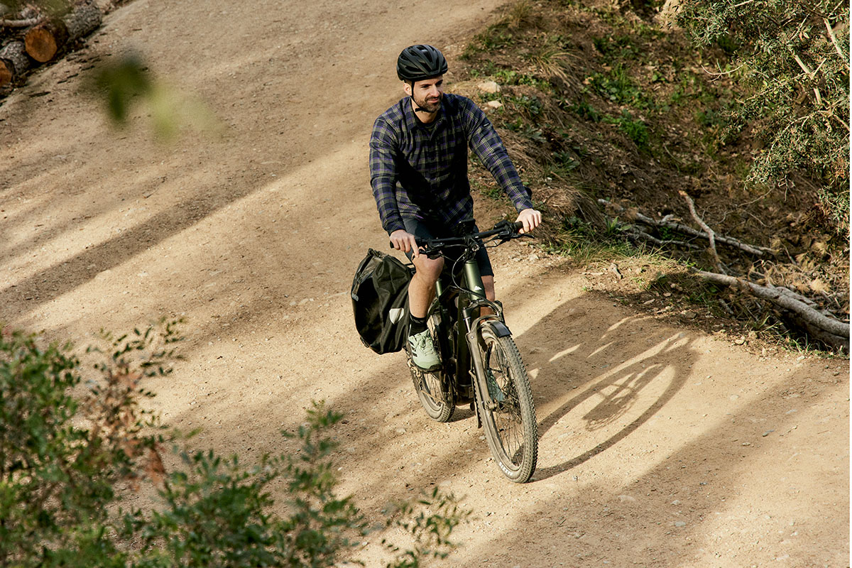 Mann fährt auf Trekking-E-Bike durch eine Parklandschaft.