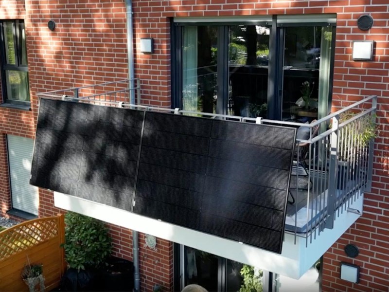 Ein Balkonkraftwerk mit zwei Solarpanels an einem Balkongitter eines Backstein-Wohnhauses.