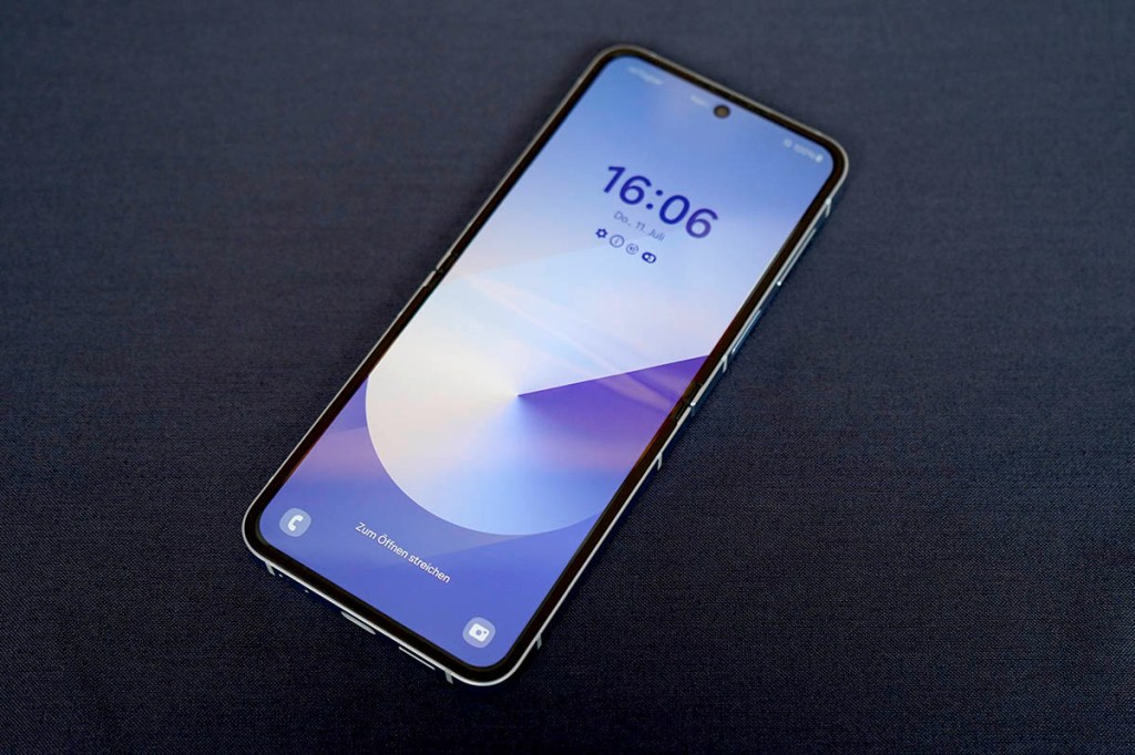 Das Klapp-Smartphone Samsung Galaxy Z Flip6 liegt mit eingeschaltetem Display auf einer dunkelblauen Oberfläche.